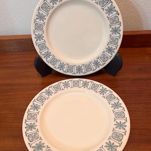 Könnte beinhalten: Zwei weiße Keramikplatten mit einem blauen Blumenmuster am Rand. Die Teller werden auf einer Holzoberfläche präsentiert. Die Teller sind rund und haben ein schlichtes, elegantes Design, das sich zum Servieren von Speisen eignet.