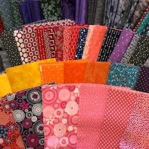 May include: A collection of fabric squares in various colors and patterns, including red, orange, yellow, pink, blue, green, and purple. The fabrics are arranged in a fan shape, with the largest squares at the bottom and the smallest squares at the top.