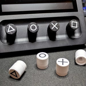 May include: Five white plastic controller caps with different symbols: triangle, circle, cross, square, and a blank cap. The caps are on a black surface.