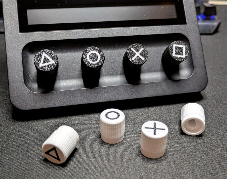 May include: Five white plastic controller caps with different symbols: triangle, circle, cross, square, and a blank cap. The caps are on a black surface.