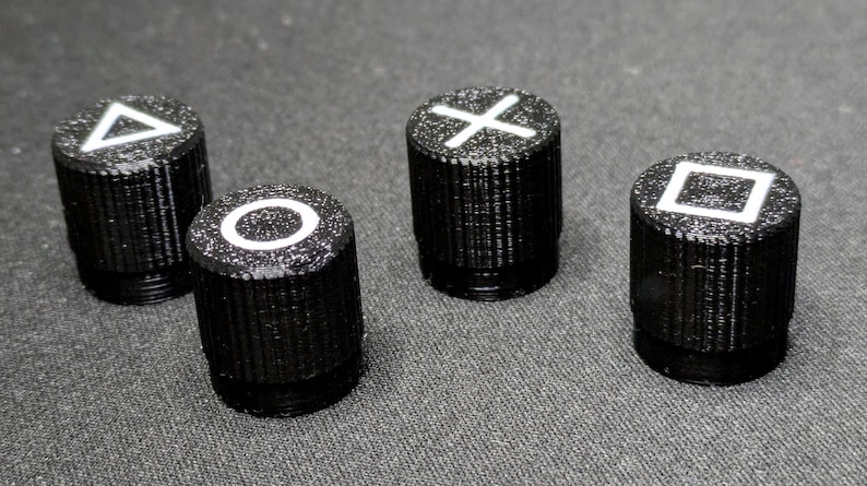 May include: Four black plastic buttons with white symbols. The symbols are a triangle, a circle, an X, and a square.