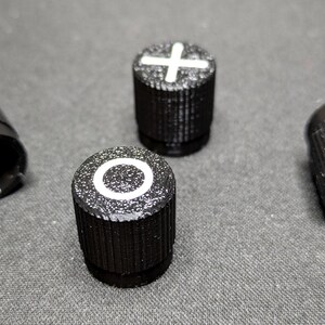 May include: Four black knobs with white symbols. The symbols are a plus sign, a circle, a square, and a blank knob.