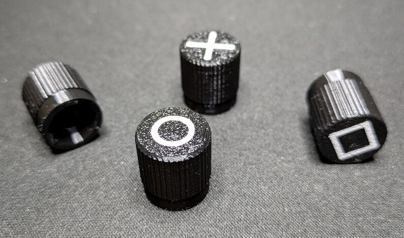 May include: Four black knobs with white symbols. The symbols are a plus sign, a circle, a square, and a blank knob.