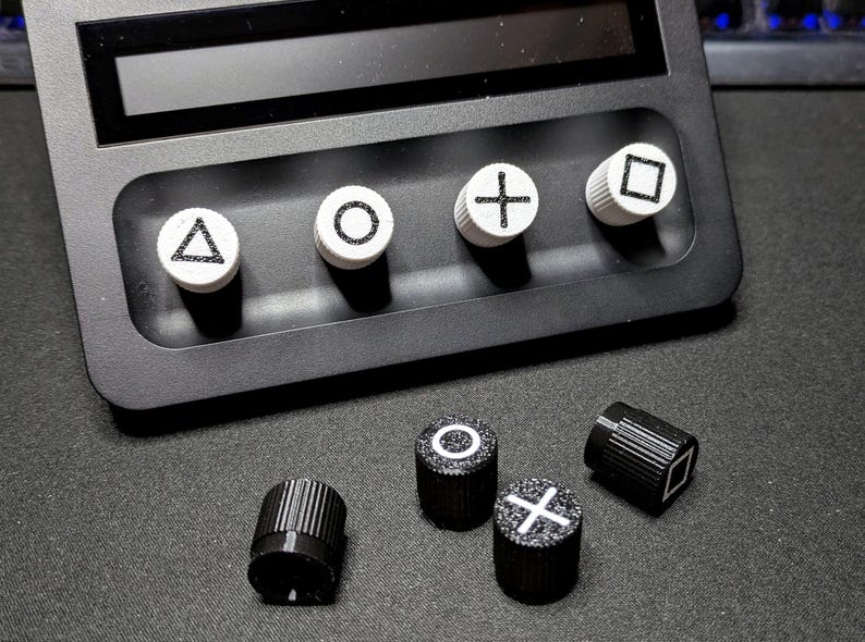 May include: A set of six black and white buttons with different symbols. The buttons are round and have a raised edge. The symbols are a triangle, a circle, a cross, a square, a circle with a dot in the center, and a cross with a dot in the center.