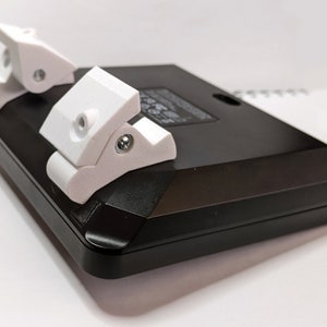 Puede incluir: Un mando de juego negro con dos accesorios de pl&aacute;stico blanco en la parte posterior. Los accesorios est&aacute;n dise&ntilde;ados para mejorar el agarre y el control.