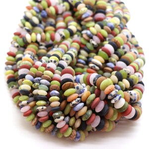 Può includere: Una collezione di piccole perline piatte e circolari in una varietà di colori tra cui verde lime, terracotta, nero, bianco, blu e motivi maculati. Le perline sono disposte in più fili, creando un ammasso denso, strutturato e molto colorato.