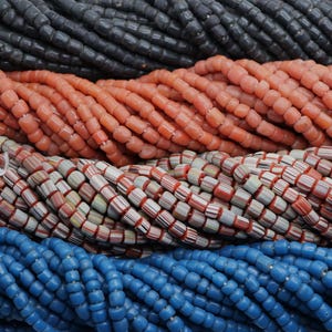 Könnte beinhalten: Nahaufnahme von Strängen bunter Perlen. Die Perlen sind in verschiedenen Farben erhältlich, darunter Schwarz, Koralle, rot-weiß gestreift und Blau. Die Perlen sind aufgefädelt und erzeugen eine strukturierte und optisch ansprechende Darstellung. Ideal für die Schmuckherstellung oder Bastelprojekte.