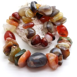 Peut inclure: Un collier de perles en pierres gemmes polies et irrégulières, présentant une variété de couleurs incluant le rouge profond, l'orange brûlé, le jaune translucide, le brun terreux et le vert foncé. Les pierres sont lisses et arrondies.