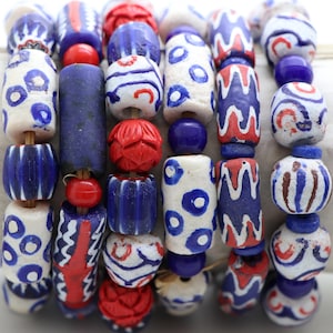 May include: A collection of multi-coloured glass beads arranged in vertical strands. The beads feature various patterns including blue and white circles, red and blue wavy lines, solid red spheres, and textured red floral shapes on a string.