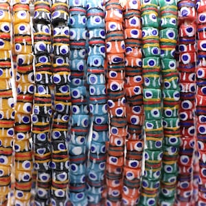 Pode incluir: Um close-up de uma coleção de contas de vidro coloridas com um padrão repetitivo de olhos azuis. As contas estão dispostas em filas e enfiadas em um cordão.