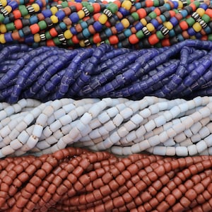 Könnte beinhalten: Nahaufnahme mehrerer Stränge bunter Perlen. Der oberste Strang zeigt eine Mischung aus schwarzen, roten, gelben, grünen und blauen Perlen. Darunter befinden sich Stränge aus blauen, weißen und braunen Perlen. Die Perlen sind klein und quadratisch.