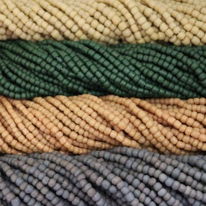 Könnte beinhalten: Nahaufnahme von vier Reihen kleiner, runder Glasperlen. Die obere Reihe ist cremefarben, die zweite Reihe dunkelgrün, die dritte Reihe hellbraun und die untere Reihe grau.