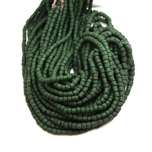 Pode incluir: Um grande feixe de contas cilíndricas verde-escuras. As contas são enfiadas, criando uma aparência densa e texturizada. As contas são de cor sólida e mate, sobre um fundo branco.