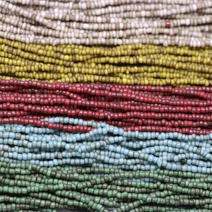 Könnte beinhalten: Nahaufnahme einer Vielzahl von bunten Glasperlen, die in Reihen angeordnet sind. Die Perlen sind klein und rund und auf einer Schnur aufgereiht. Die Farben der Perlen sind weiß, gelb, rot, blau und grün.