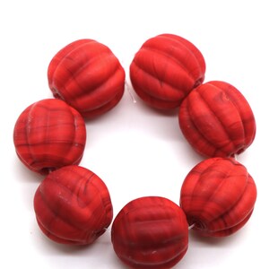 May include: A strand of red glass beads with a ribbed texture. The beads are round and have a slightly marbled appearance.