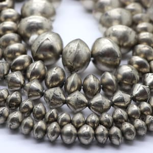 Può includere: Una collana di perline argentate con forma arrotondata e sfaccettata. Le perline sono disposte in un mucchio sciolto, mostrando il loro design unico.