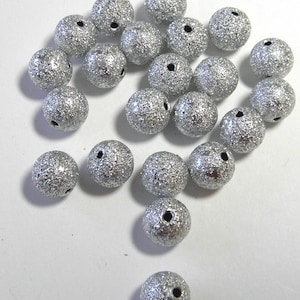 Op de afbeelding: Een verzameling zilveren glitter kralen met een gat in het midden. De kralen zijn rond en hebben een getextureerd oppervlak.