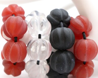 May include: A close-up of a bracelet made with three colors of beads: red, clear, and black. The beads are all round and have a textured surface. The bracelet is strung on a black elastic cord.