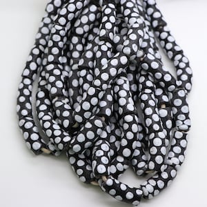 May include: A collection of black and white polka dot beads. The beads are cylindrical, with a dark base and white polka dots. They are strung together, potentially forming a necklace or bracelet.