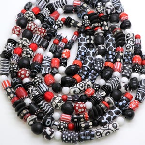 May include: A selection of handmade beads in diverse shapes and sizes. The beads are mainly black, white, and red, featuring patterns like stripes, polka dots, and geometric designs. Some beads are solid, while others have intricate patterns.