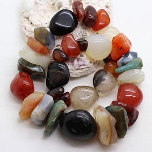 May include: A collection of polished, tumbled stones in various shapes and sizes, featuring a diverse color palette including deep black, vibrant orange, translucent white, muted green, and soft gray, arranged in a circular cluster formation.