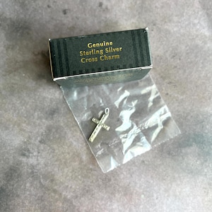 May include: A small silver cross charm in a clear plastic bag with a black and gold striped box that says "Genuine Sterling Silver Cross Charm".