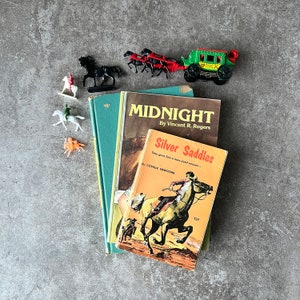 May include: Three vintage paperback books with colorful covers. The top book is titled "Midnight" by Vincent R. Rogers. The middle book is titled "Silver Saddles" by Covelle Newcome. The bottom book has a colorful illustration of a horse and rider.