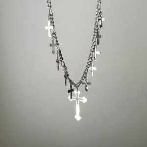 May include: A silver chain necklace with multiple small cross charms. The necklace has a larger cross charm at the bottom.
