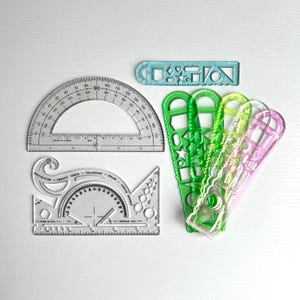 May include: A set of clear plastic geometry tools, including a protractor, a ruler, and several stencils. The stencils feature various shapes, including circles, squares, triangles, and stars. The tools are all transparent and have black markings.
