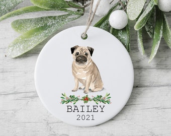 May include: White ceramic Christmas ornament featuring a pug dog illustration with a green holly wreath and the text "BAILEY 2021".
