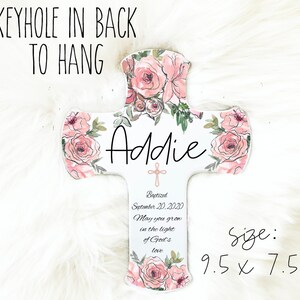 May include: A white wooden cross decorated with pink watercolor roses and green leaves. The name "Addie" is written in black script. The cross is 9.5 x 7.5 inches and includes the text "Baptized September 20, 2020" and "May you grow in the light of God's love."