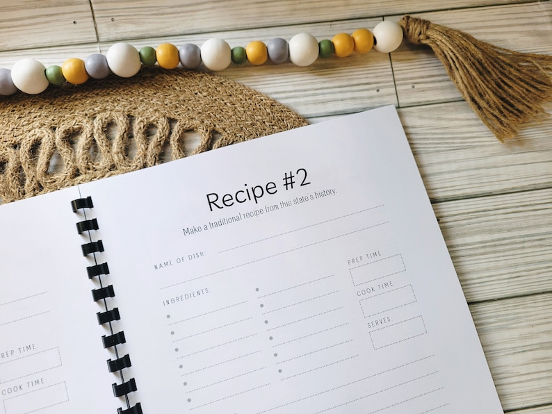 May include: A white recipe book with a black spiral binding. The book has a title that reads "Recipe #2" and the text "Make a traditional recipe from this state's history." The book has sections for the name of the dish, ingredients, prep time, cook time, and servings.