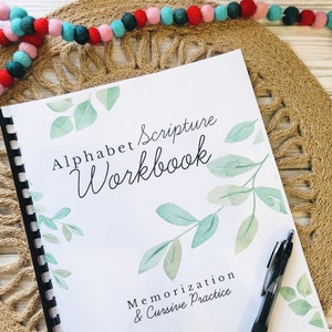 May include: A white alphabet scripture workbook with a green watercolor leaf design. The title is "Alphabet Scripture Workbook" and the subtitle is "Memorization & Cursive Practice".