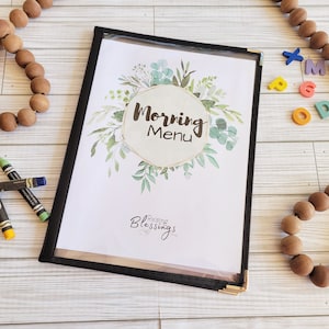 May include: A black menu holder with a clear plastic cover, displaying a "Morning Menu" with floral accents. The menu is surrounded by wooden beads, crayons, and colorful letter blocks.