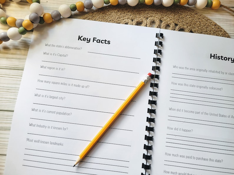 May include: A blank notebook with a spiral binding and lined pages. The notebook is open to a page with the title "Key Facts" and a list of questions about a state. The next page is titled "History" and has questions about the history of a state. A yellow pencil is lying on the notebook.