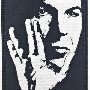 Puede incluir: Parche bordado en blanco y negro con un retrato de primer plano de una cara con la mano cubriendo parte de la cara.