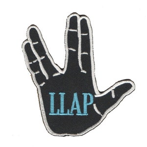 Puede incluir: Un parche bordado negro con un contorno blanco de una mano haciendo el saludo Vulcano. La mano tiene el texto "LLAP" en bordado azul en la palma.