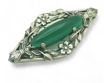 May include: A silver brooch with a green stone set in a floral design.