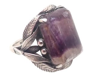 May include: A silver ring featuring a large, rectangular purple gemstone. The ring has a decorative design with silver leaves and small silver beads. The gemstone has a polished surface and a mix of purple and white hues.