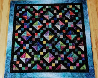 May include: A colorful quilt with a geometric pattern of diamonds and squares. The quilt is made of various fabrics in shades of blue, green, red, yellow, and black. The quilt is edged with a blue border.