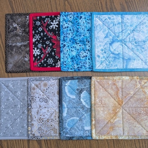 May include: Eight different square pot holders with various patterns. The pot holders are made of fabric and have a quilted design. The patterns include a blue and white floral design, a brown and white marble design, a black and white design with red reindeer, a blue and white geometric design, a brown and white geometric design, a gray and white geometric design, a brown and white polka dot design, and a blue and white floral design.