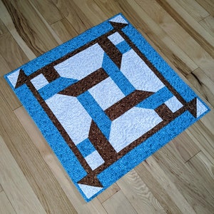 May include: A blue and brown patchwork quilt with a geometric design. The quilt is made of squares and rectangles, and the colors are arranged in a repeating pattern.
