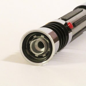 May include: A silver and black lightsaber toy with a red button. The lightsaber has a detailed design and a black ring around the end.