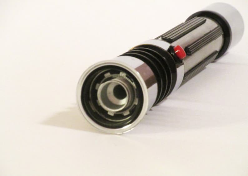 May include: A silver and black lightsaber toy with a red button. The lightsaber has a detailed design and a black ring around the end.