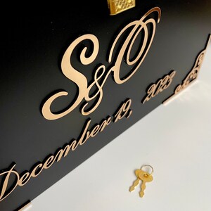 May include: Black wooden box with a gold lock and key. The box has a gold inscription that reads "S&O December 19, 2023".