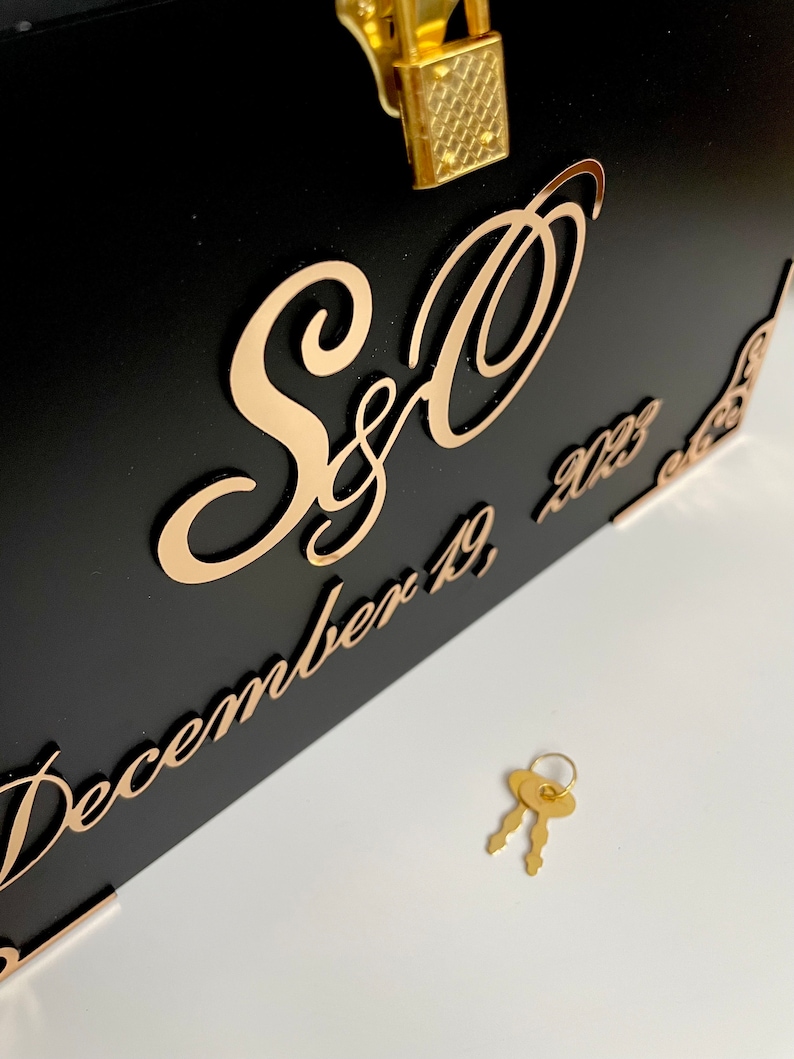 May include: Black wooden box with a gold lock and key. The box has a gold inscription that reads "S&O December 19, 2023".