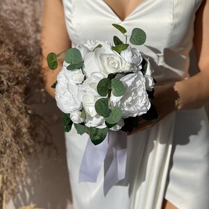 May include: A white bridal bouquet with white roses and greenery.