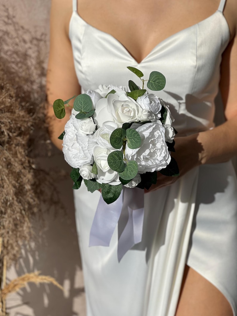 May include: A white bridal bouquet with white roses and greenery.