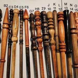 May include: A collection of 16 wooden wands, each with a unique design and finish. The wands are arranged in a row, with the tips pointing to the right. The wands are made of different types of wood, including dark brown, light brown, and natural wood.