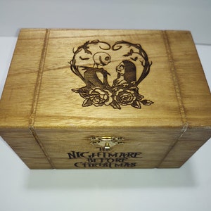 May include: A wooden box with a hinged lid. The lid is decorated with an engraved image of Jack Skellington and Sally from the movie "The Nightmare Before Christmas". The box is labeled "The Nightmare Before Christmas".